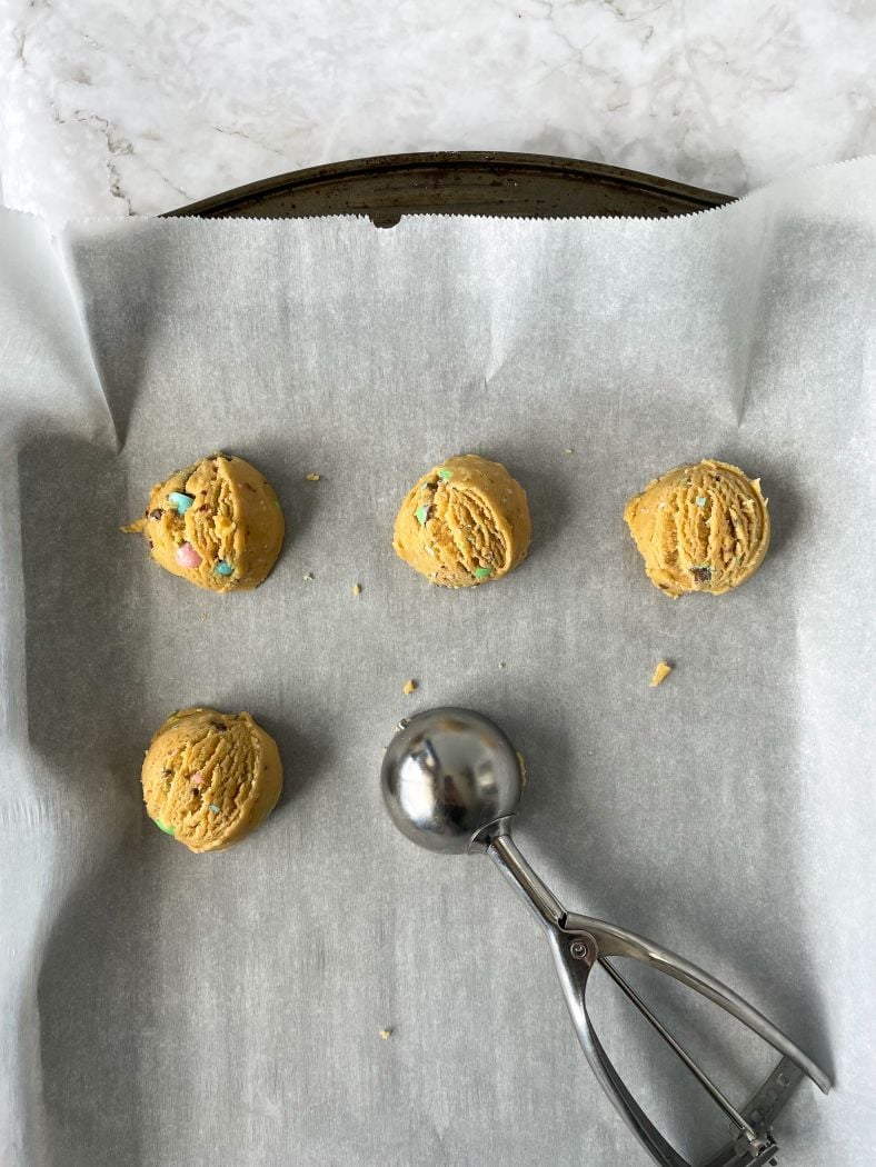 cookie scooping the dough into cookie dough balls on a lined baking sheet